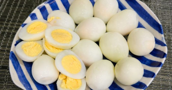 Đĩa trứng luộc bóc vỏ với vài nửa quả để lộ lòng đỏ và lòng trắng trên đĩa sứ sọc xanh trắng.