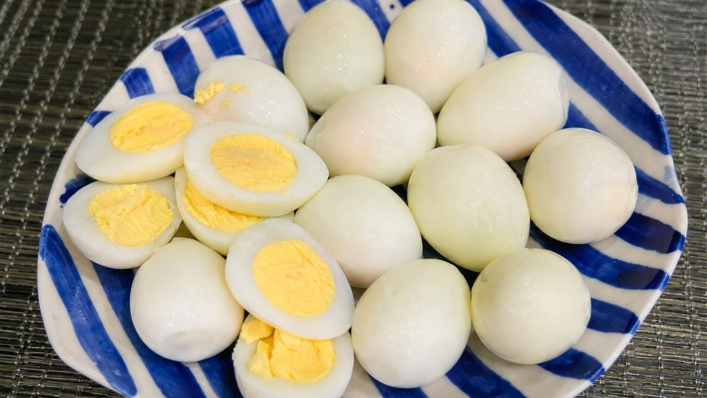 Đĩa trứng luộc bóc vỏ với vài nửa quả để lộ lòng đỏ và lòng trắng trên đĩa sứ sọc xanh trắng.